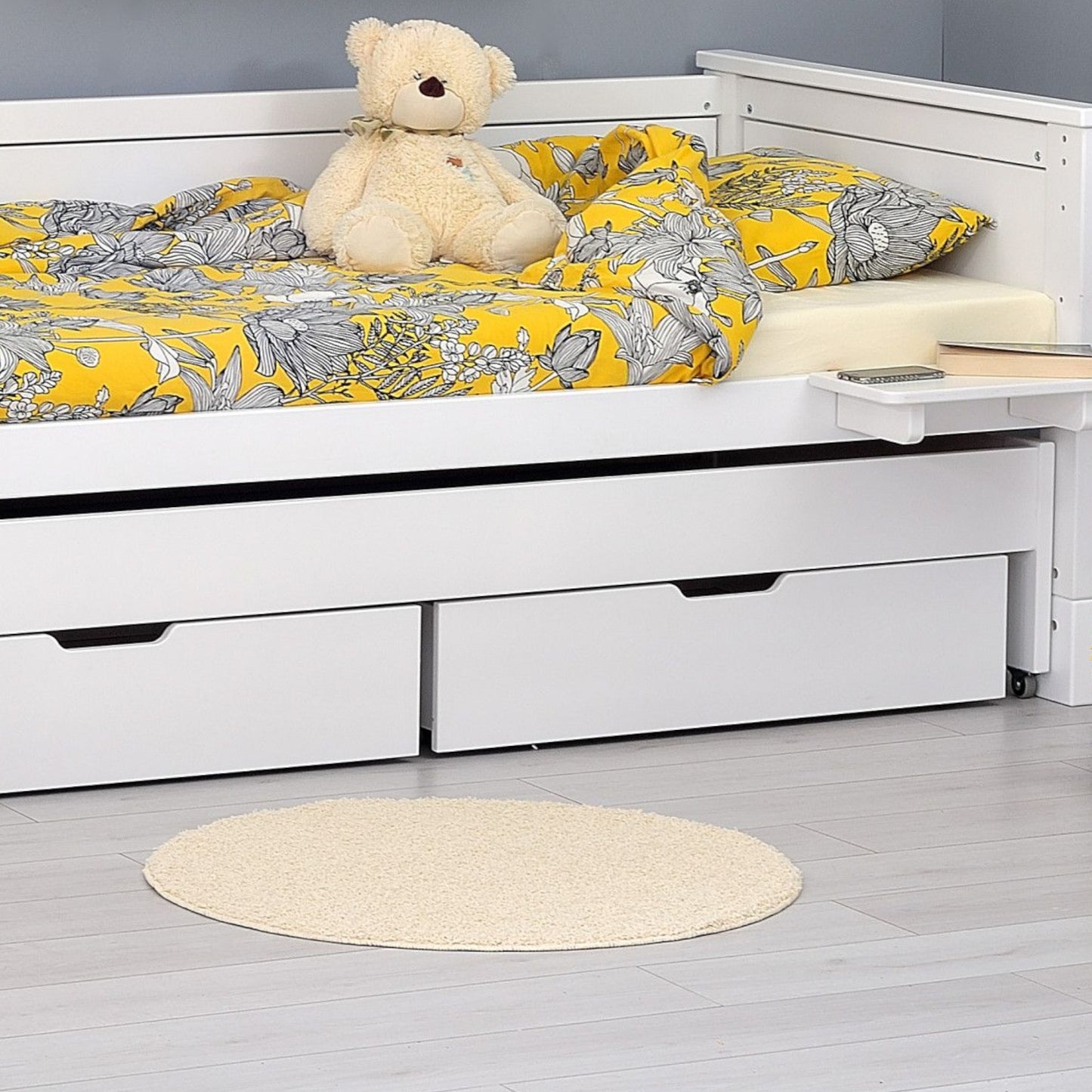 Jerwen - Bed drawer - 90x75x21 cm under a bed with a yellow floral bedding and a teddy bear.