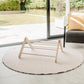 Round beige rug with a wooden stool in a modern living room with large glass doors.