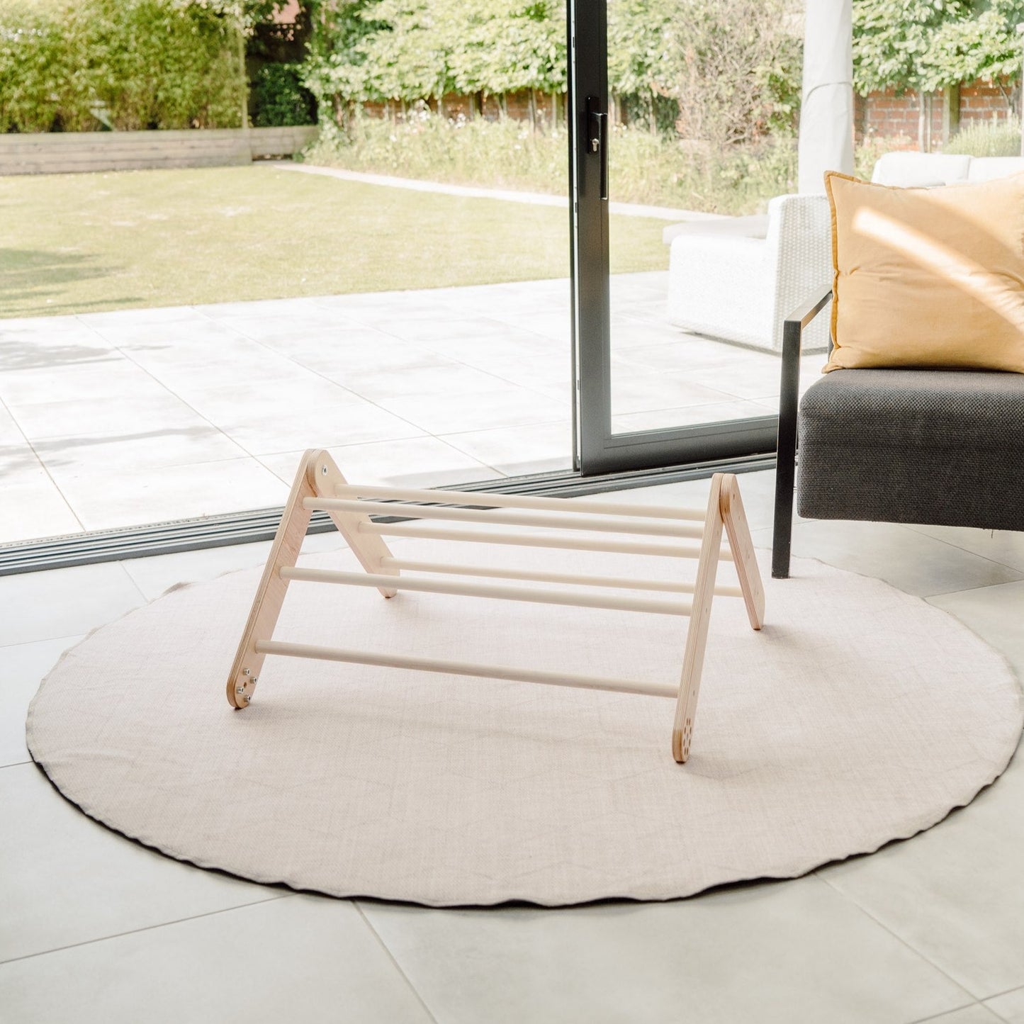 Round beige rug with a wooden stool in a modern living room with large glass doors.