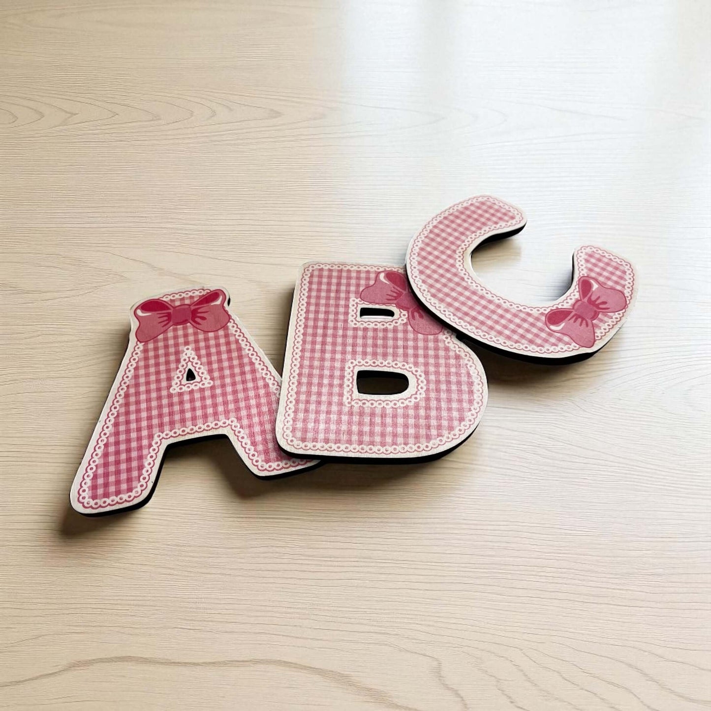 Pink checkered letters 'A', 'B', and 'C' on a wooden surface