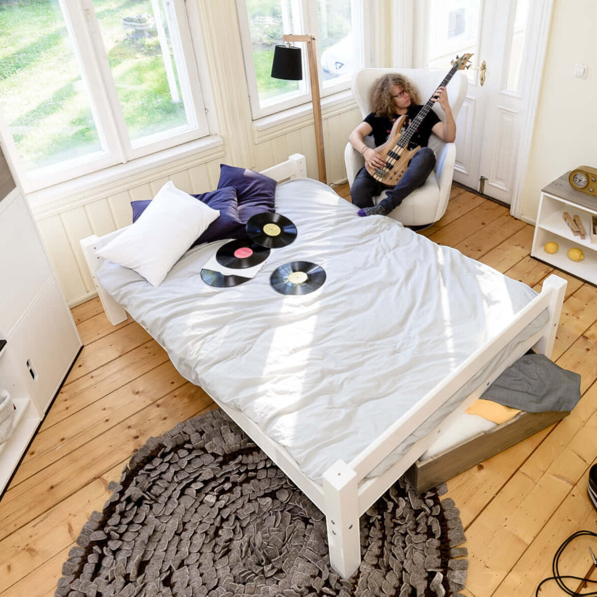 Lahe - Bed - 140x200 cm - White in a stylish room with a person playing guitar and vinyl records on the bed.