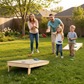 Family enjoying a game of Cornhole Board - 120x60 cm in the backyard during a sunny day.