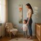 A mother measuring her child's height with a Kids measuring stick on the wall in a cozy nursery.